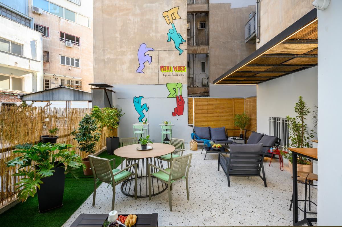 Shared balcony at Psiri Vibes Hotel featuring outdoor seating, plants, and colorful wall art.